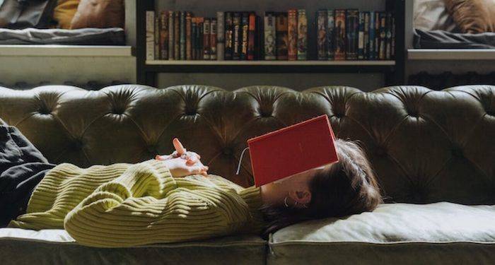 a photo of a woman lying on a couch with a book over her face